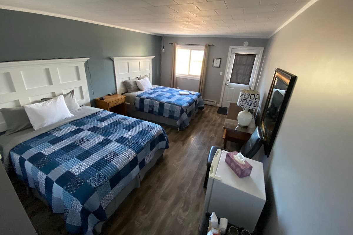 Habitación de hotel con dos camas, una mesita, una silla, un escritorio y un espejo.
