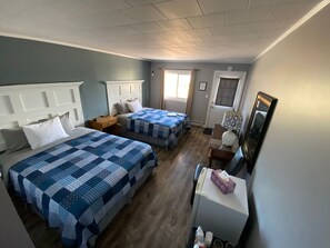 Quarto de hotel com duas camas, uma mesinha, uma cadeira, uma escrivaninha e um espelho.