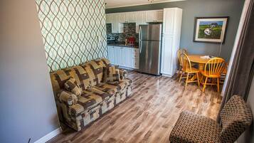 Una sala de estar acogedora con un sofá estampado, una zona de comedor con sillas de madera y una cocina con alacenas blancas y un refrigerador de acero inoxidable.