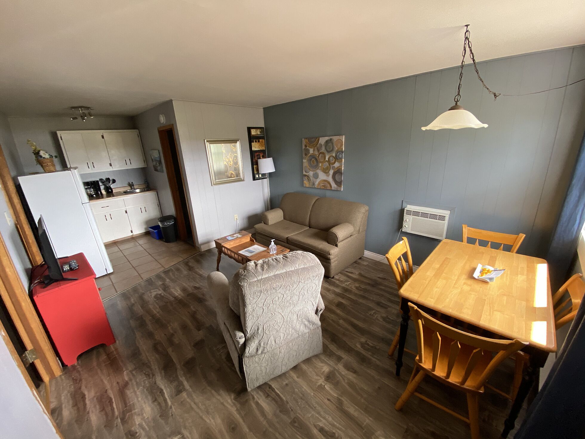 A compact living space with a kitchenette, a sofa, a dining table, and a small red cabinet.