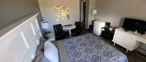 A hotel room with a bed, a desk, a chair, a TV, and a small table.
