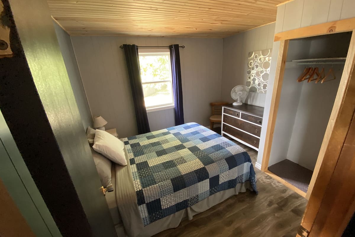 Un dormitorio con cama, cómoda, ventana con cortinas y techo de madera.