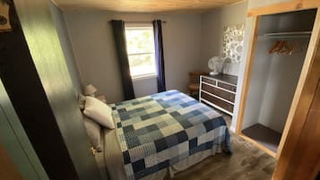 A bedroom with a bed, a dresser, a window with curtains, and a wooden ceiling.