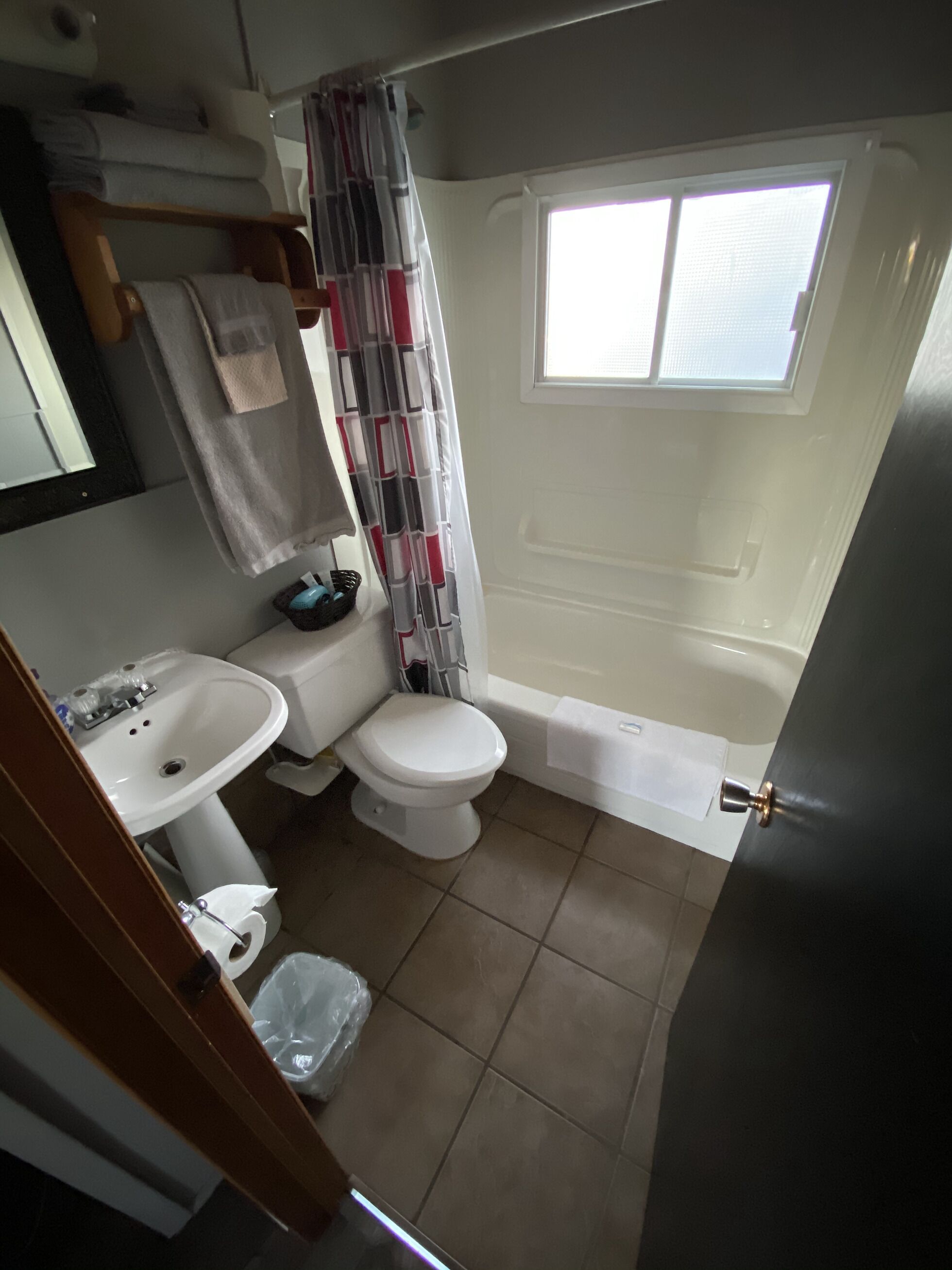 A compact bathroom with a white sink, toilet, and bathtub. A window provides natural light, and a curtain covers the shower area.