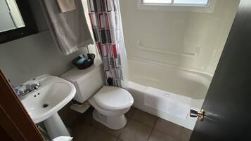 A compact bathroom with a white sink, toilet, and bathtub. A window provides natural light, and a curtain covers the shower area.