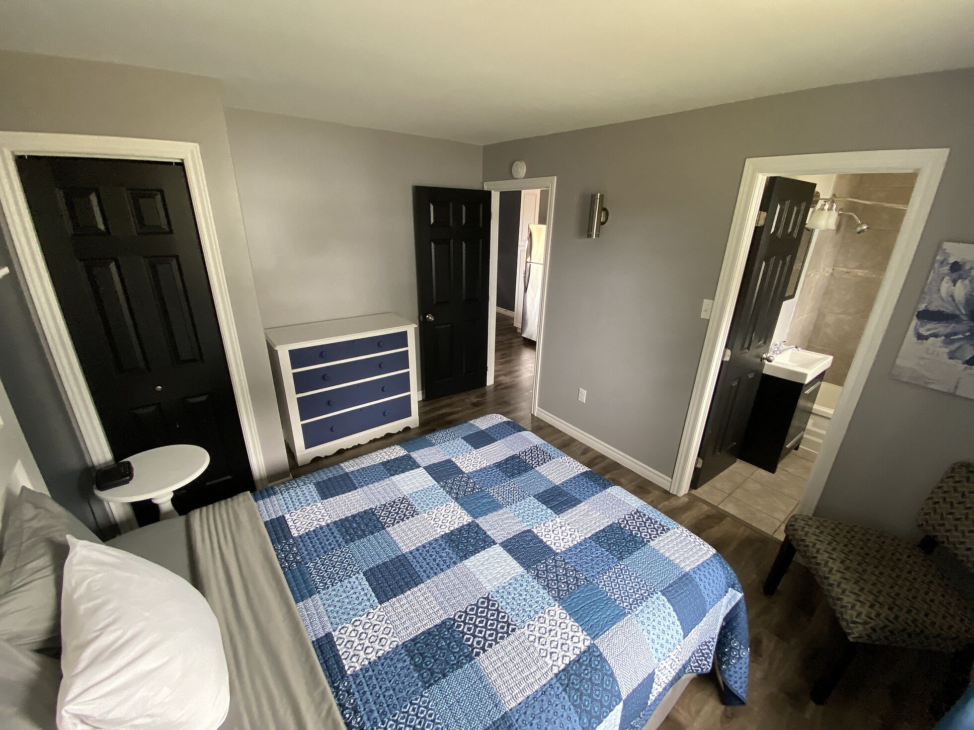 A bedroom with a bed, a dresser, a chair, and a bathroom visible through an open door.