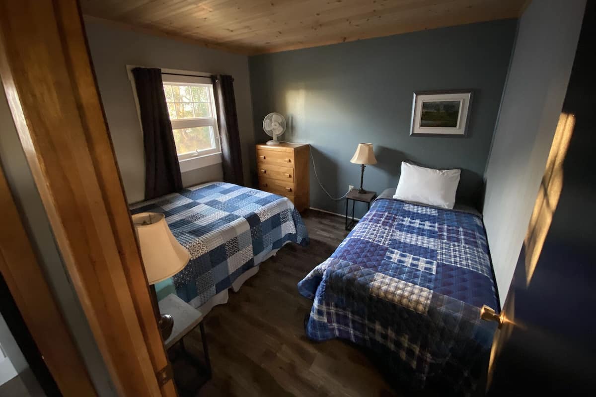 Un dormitorio con dos camas, un aparador, una mesita de noche, una ventana con cortinas y un cuadro colgado en la pared.