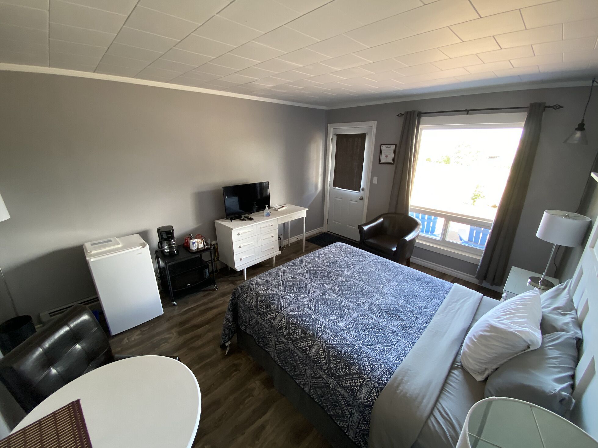 A hotel room with a bed, a desk with a computer, a chair, a small table, and a window with a view of the outside.