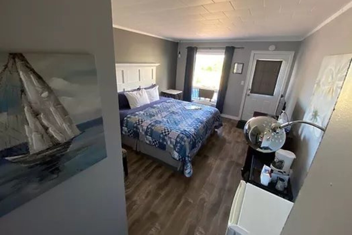 A bedroom with a bed, a bedside table, a mirror, and a door.