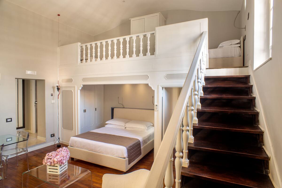 Een slaapkamer met een tweepersoonsbed, een glazen salontafel, een stoel, een dressoir en een trap.