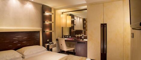 A hotel room with a large bed, a desk, a chair, a refrigerator, and a mirror.