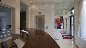 Eine moderne Hotellobby mit einer gebogenen Rezeption, einem Glaselevator und freiem Blick auf den Essbereich im Hintergrund.