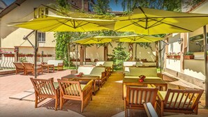 Eine Terrasse im Freien mit Holztischen und -stühlen, gelben Sonnenschirmen und Kübelpflanzen.