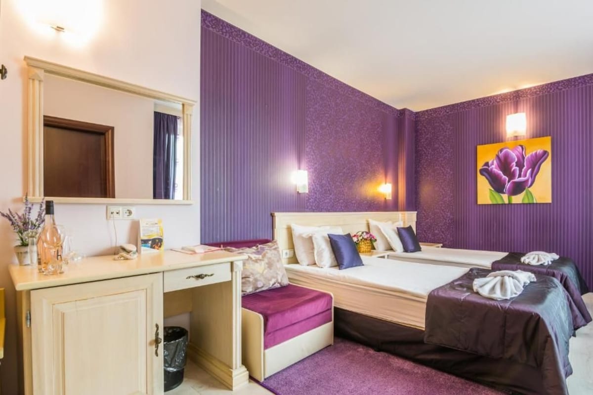 A hotel room with a bed, bedside tables, a desk, and a large mirror.