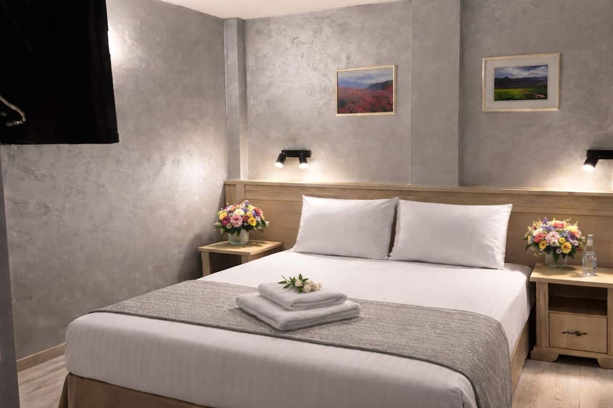 A hotel room with a bed, two nightstands with flower vases, a wooden headboard, and two framed pictures on the wall.