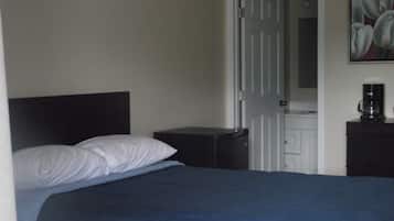 Quarto com cama, mesa de cabeceira, máquina de café e porta para outro cômodo.