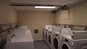 Un cuarto de lavandería con varias lavadoras y secadoras, un sistema de ventilación y una lámpara fluorescente.