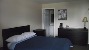 Un dormitorio con cama, cómoda, cafetera y un cuadro en la pared.