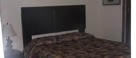 Un lit avec une couvre-lit à motifs, une tête de lit sombre, une table de chevet avec une lampe et un tableau encadré au mur.