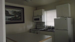 Una pequeña cocina con armarios blancos, un microondas, una estufa y un refrigerador.