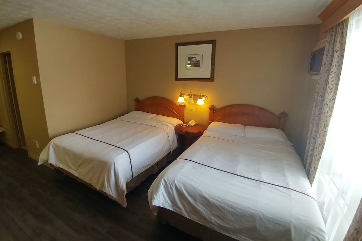 A hotel room with two single beds, a wooden headboard, a bedside table with a lamp, and a framed picture on the wall.