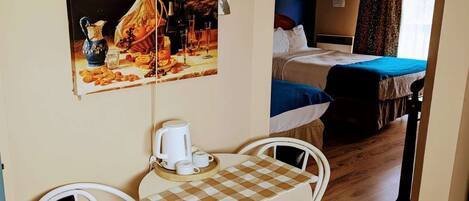 A small room with a bed, a table with chairs, and a painting on the wall.