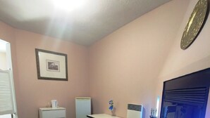 Una habitación con un sofá de cuero negro, una mesita blanca con un jarrón, un armario blanco, un calentador y un espejo grande.