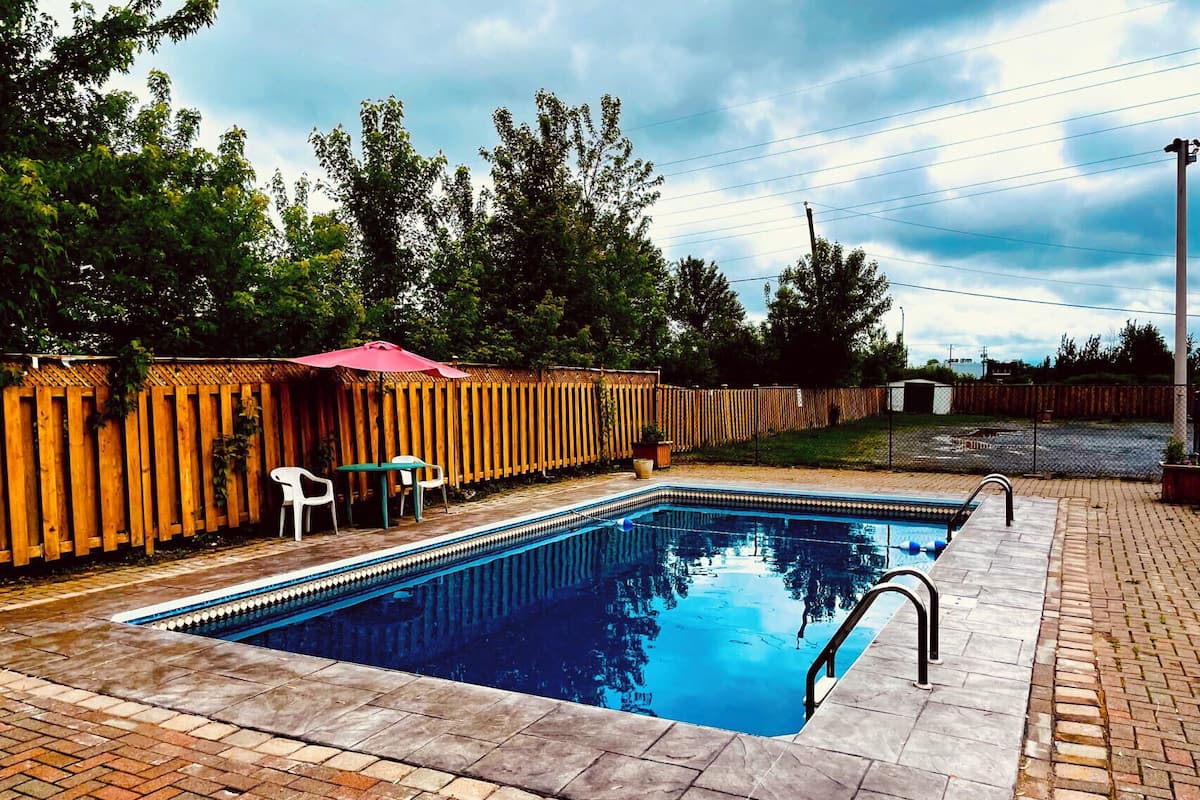 A rectangular swimming pool with a tiled deck, surrounded by a wooden fence and a brick patio.