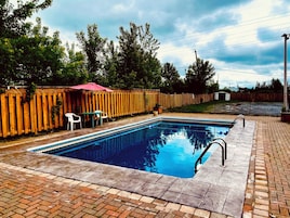 Una piscina rectangular con solárium azulejado, rodeada por una cerca de madera y un patio de ladrillo.