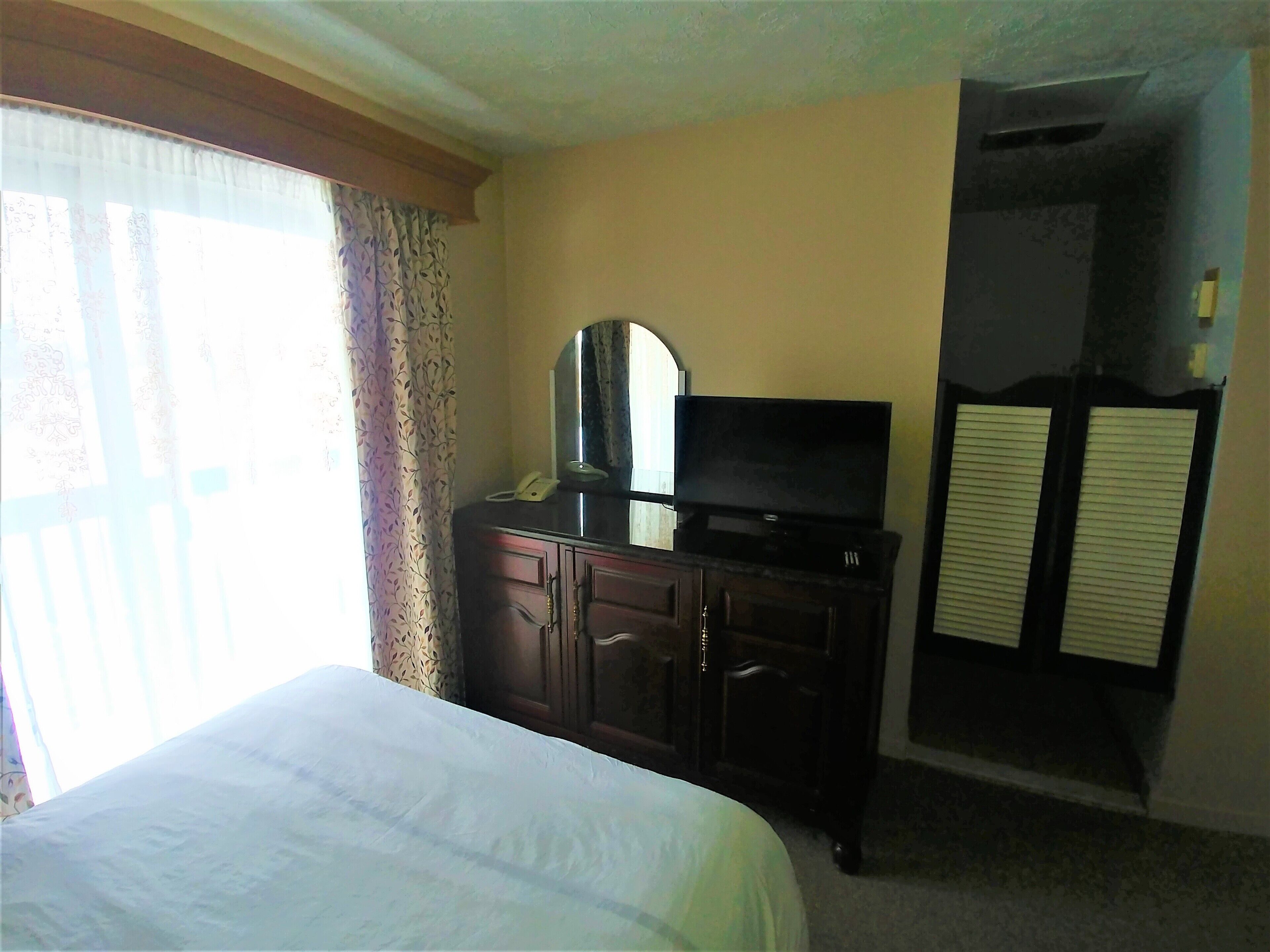 A hotel room with a bed, a dresser with a television, and a mirror.