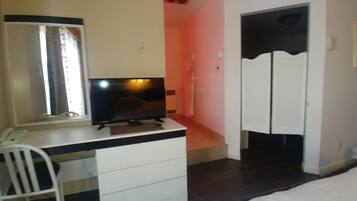 A bedroom with a bed, a desk with a chair, a television, and a wardrobe.