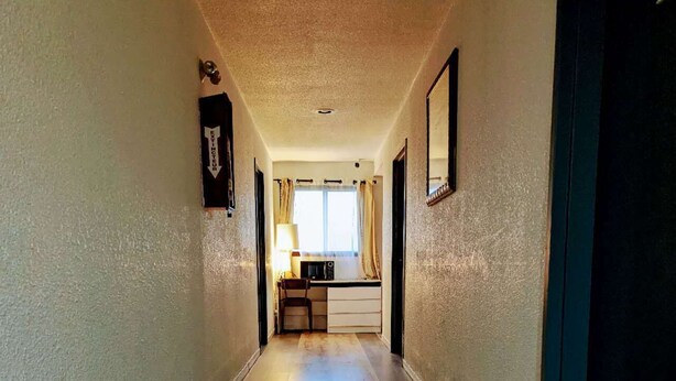 Un pasillo de hotel con piso de madera, un escritorio con lámpara y una ventana con cortinas.