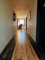 Un pasillo de hotel con piso de madera, un escritorio con lámpara y una ventana con cortinas.