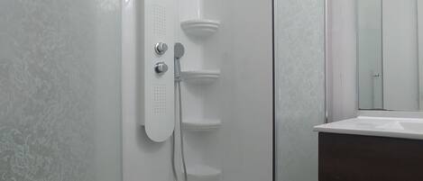 Ducha con cerramiento de vidrio, cabezal de ducha manual y un estante pequeño.