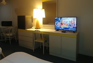 Una habitación de hotel con cama, escritorio con lámpara, televisión y una silla.