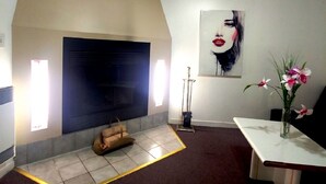 Una habitación con chimenea, ventilador de techo, un cuadro grande y un jarrón con flores.