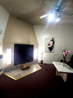 Una habitación con chimenea, ventilador de techo, un cuadro grande y un jarrón con flores.