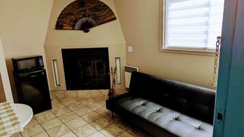 A living room with a black sofa, a small table, a microwave, a fireplace, and a fan on the wall.