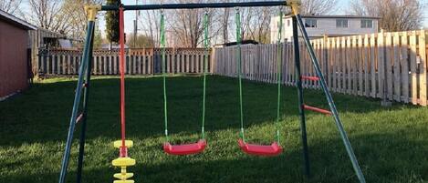 A swing set in a backyard with a wooden fence and a house in the background.