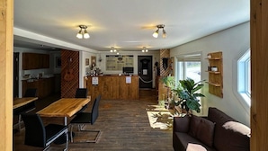 A cozy interior with a wooden dining table, black chairs, a sofa, and a kitchen area in the background. - Auberge du Lac Malcom (Sayabec)