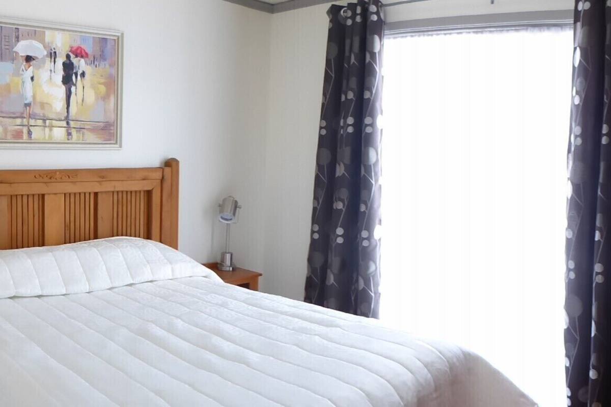 Uma cama bem arrumada com cabeceira de madeira, luminária ao lado e um quadro na parede acima.