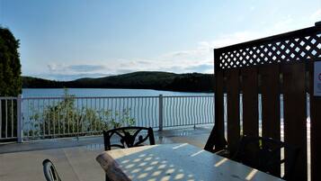 A wooden table and chairs on a terrace with a view of a lake and forest.