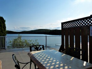 A wooden table and chairs on a terrace with a view of a lake and forest. - Auberge du Lac Malcom (Sayabec)