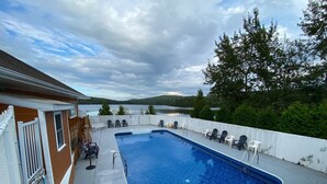 A rectangular swimming pool with a white deck, surrounded by a white fence and trees. - Auberge du Lac Malcom (Sayabec)