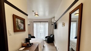 A hotel room with a bed, a desk with a laptop, a chair, a TV, and a large mirror. - Auberge du Lac Malcom (Sayabec)