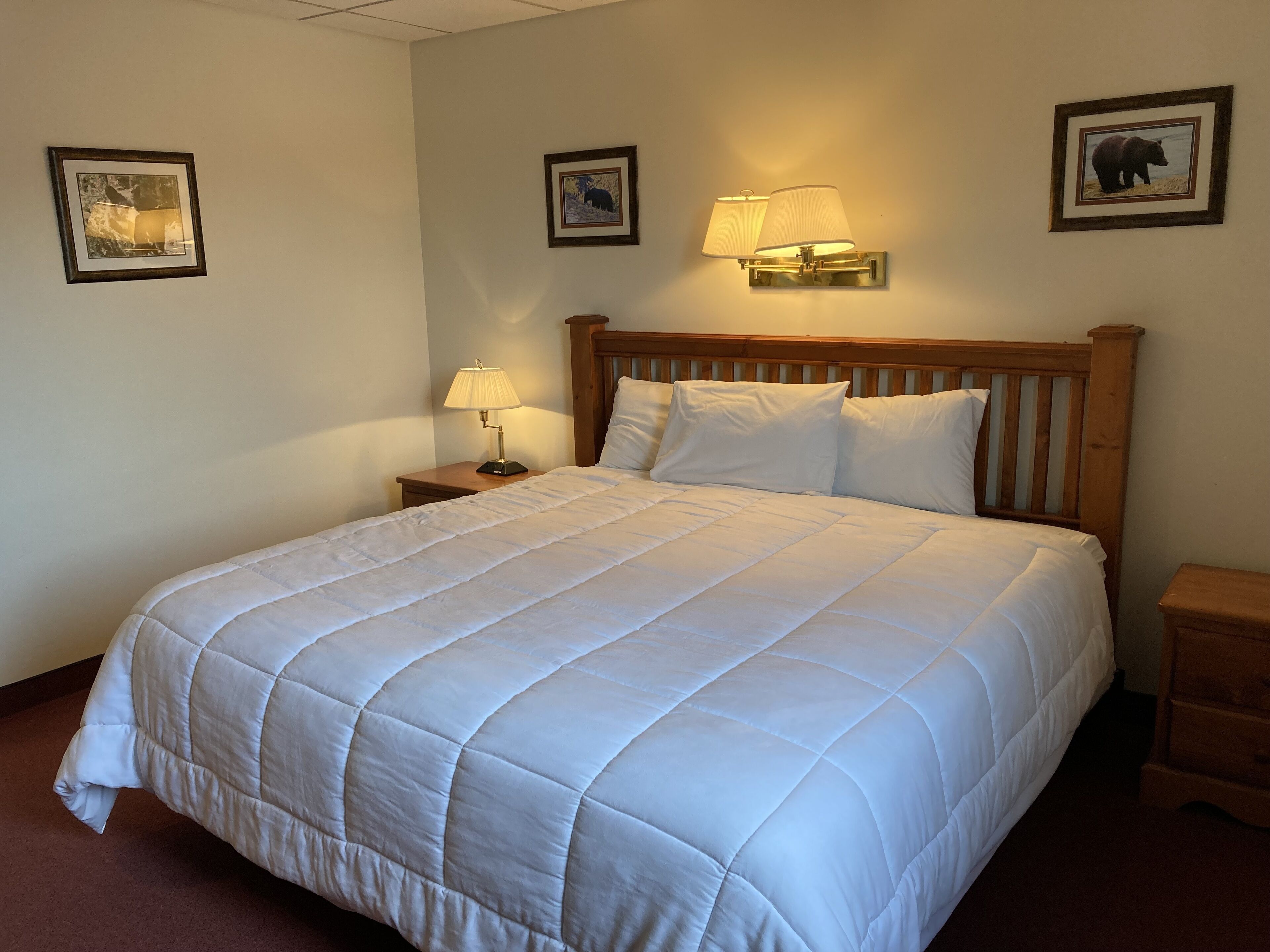 A neatly made bed with a quilted white comforter, a wooden headboard, and two bedside lamps.