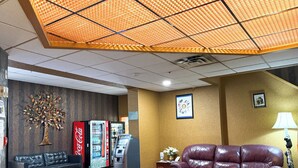 A lobby with a sofa, a Coca-Cola refrigerator, an ATM, a wall-mounted clock, and a lamp.