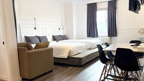 A modern hotel room with a bed, a sofa, a dining table, and a TV.