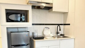 A compact kitchen with white cabinetry, a stainless steel refrigerator, a microwave, a coffee maker, and a sink.