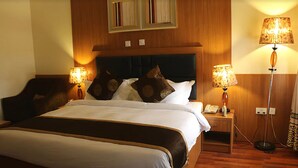 Una habitación de hotel con una cama grande, dos lámparas de noche, una mesita de noche con teléfono y un cabecero de madera.